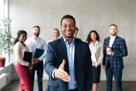Employment. Successful African American Businessman Stretching Hand For Handshake Greeting Standing With Employees Team In Modern Office, Smiling To Camera. Career Offer Concept. Selective Focus